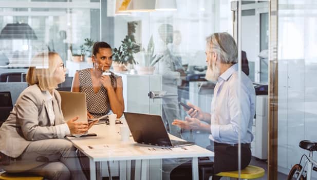 looking into glass office where 3 people are having a meeting